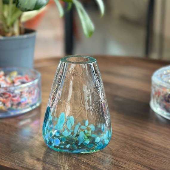 Стеклянная ваза с синими камнями на деревянном столе в комнате с растениями и цветами