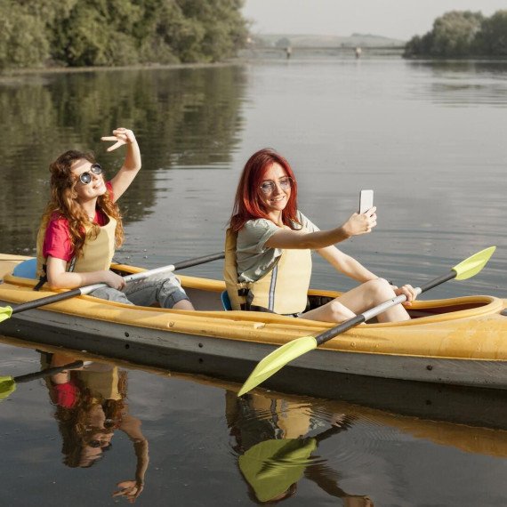 Две девушки катаются на каяке и делают селфи на реке в солнечный день. Главное фото