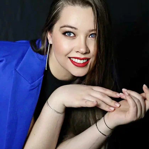 Модель с длинными волосами и яркой улыбкой в синем пиджаке на черном фоне во время фотосессии