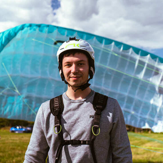 Парапланерист в спортивном костюме готовится к полету на фоне яркого параплана и облачного неба на открытом поле