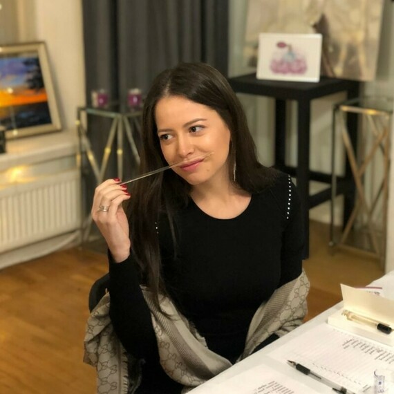 Женщина с улыбкой и ручкой в руках сидит за столом, обсуждая проекты в уютном помещении, наполненном искусством. Фото 5