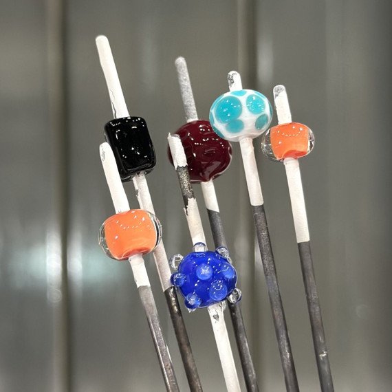 Стеклянные бусины на стержнях в мастерской по изготовлению стеклянных изделий Стеклянные бусины на стержнях в мастерской по изготовлению стеклянных изделий