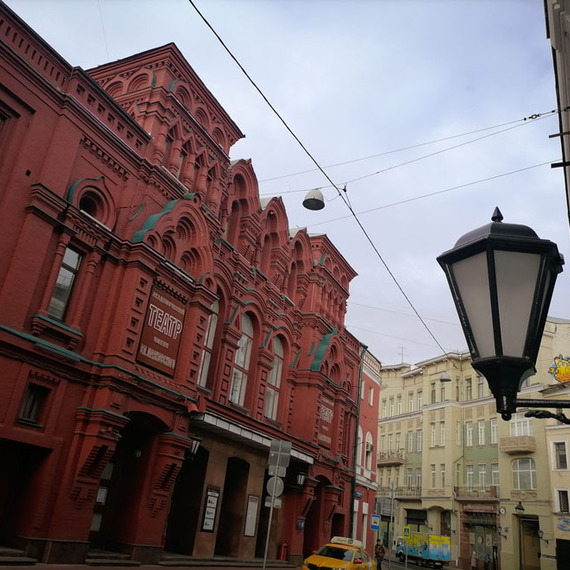 Здание театра на улице в Москве, яркая красная архитектура среди серых домов и пасмурное небо. Фото 10