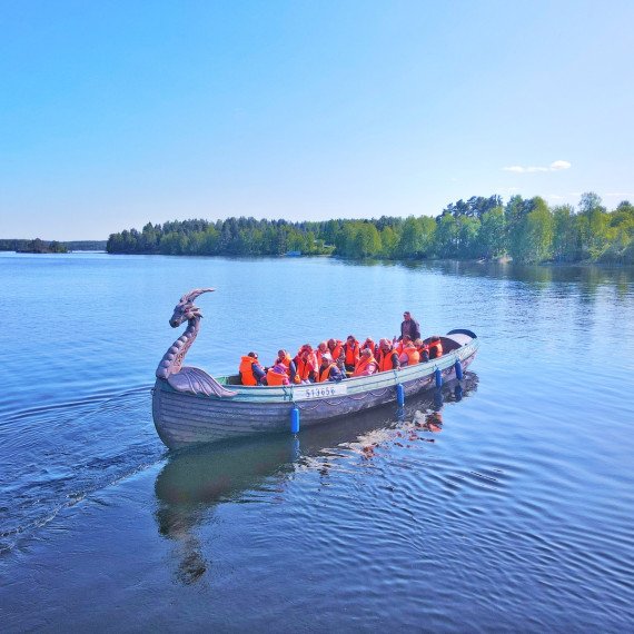 Группа людей в лодке в форме дракона на спокойном озере в солнечный день