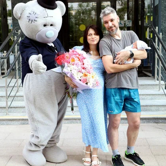 Счастливые родители с новорожденным ребенком у больницы, рядом с медвежонком в костюме, в летний день. Фото 7