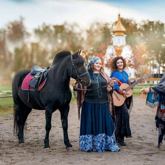 Женщины в традиционной одежде с лошадью на лугу рядом с историческим зданием