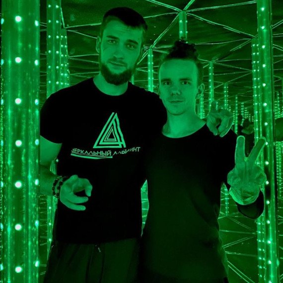 Два человека позируют в зеркальном лабиринте под зелёным светом