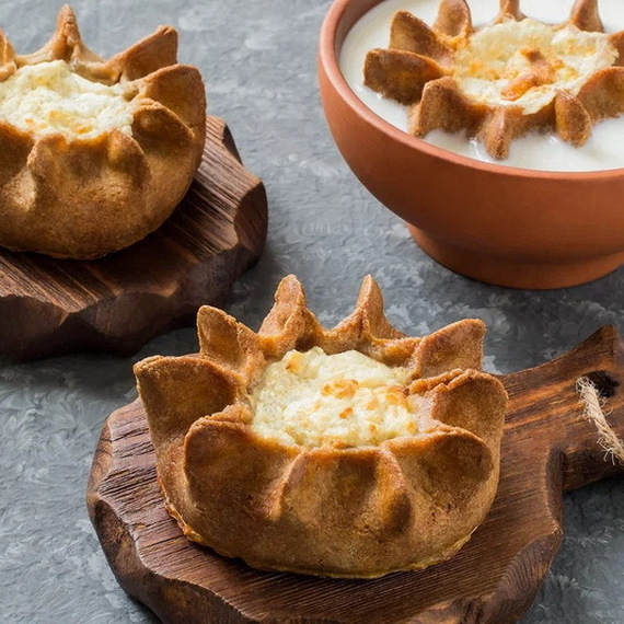 Вкусные вареники с начинкой на деревянной разделочной доске и тарелка сметаны на столе. Фото 8