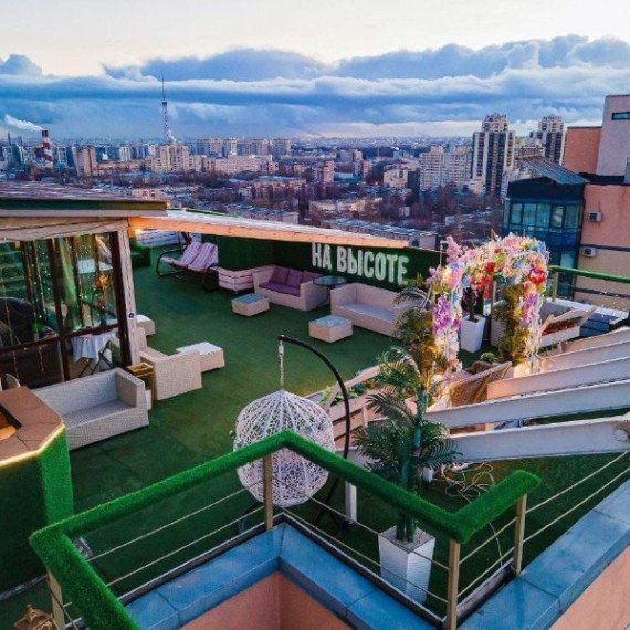 На крыше высотного здания расположена зона для отдыха с мягкой мебелью и зелеными растениями