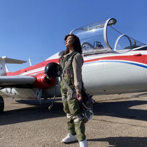 Пилот в костюме стоит рядом с самолетом на фоне ясного неба