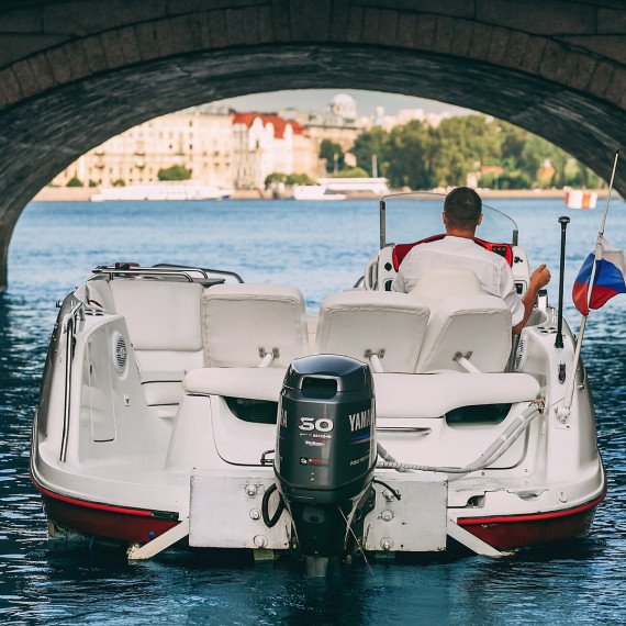 Человек на моторной лодке проходит под мостом в спокойной реке на фоне города