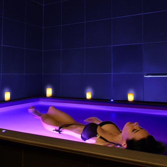 Женщина плавает в светлой воде в спа с мягким освещением в вечерние часы. Главное фото