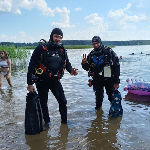Два дайвера на мелководье озера в ясный солнечный день, готовящиеся к погружению в водоем Два дайвера на мелководье озера в ясный солнечный день, готовящиеся к погружению в водоем