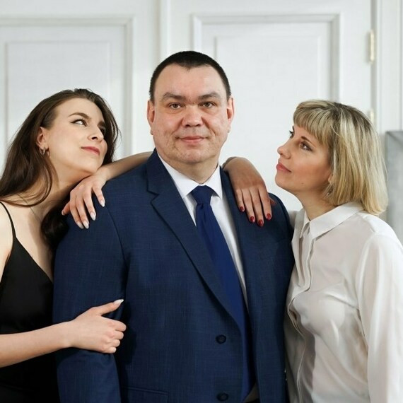 Две женщины обнимают мужчину в деловом костюме в светлом помещении на фоне абстрактного искусства. Фото 4