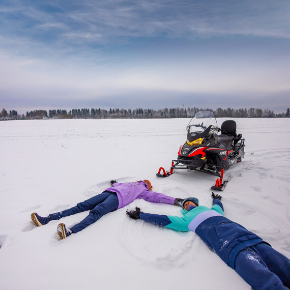 Два человека лежат в снегу рядом с снегоходом на зимнем поле
