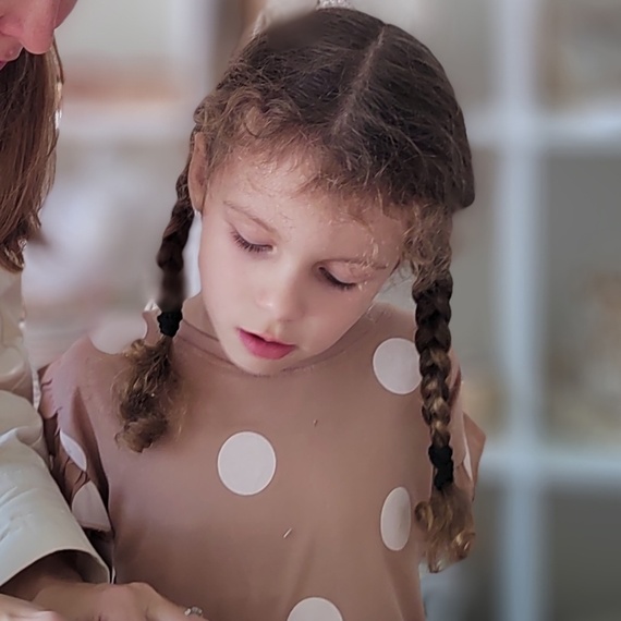 Девочка с косичками увлеченно рисует на столе рядом с взрослым в уютной комнате