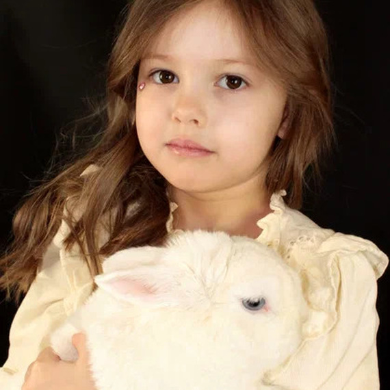 Девочка с длинными волосами нежно держит белого кролика на черном фоне в уютной атмосфере Девочка с длинными волосами нежно держит белого кролика на черном фоне в уютной атмосфере