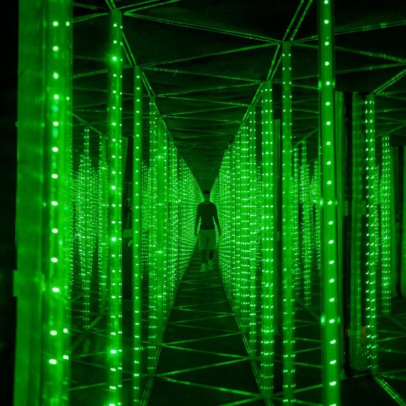 Пешеход гуляет по зеленому коридору с LED огнями в темном помещении. Главное фото