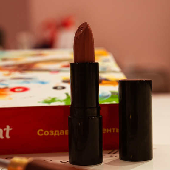 Помада в черном корпусе на столе с яркой упаковкой в мягком освещении Помада в черном корпусе на столе с яркой упаковкой в мягком освещении