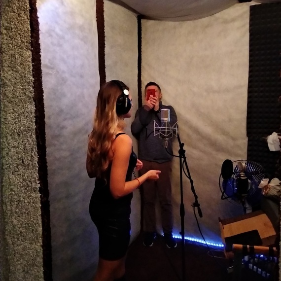 Запись песни в студии звукозаписи, девушка поет в наушниках, а парень снимает на телефон