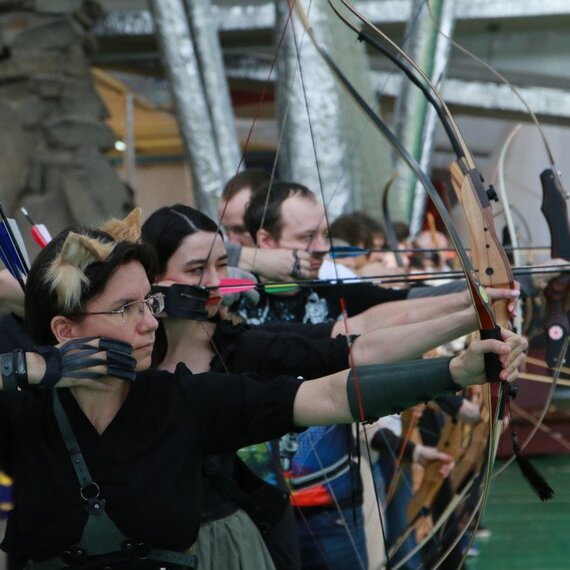 Стрельба из лука на турнире в помещении с участниками и стрелами на фоне