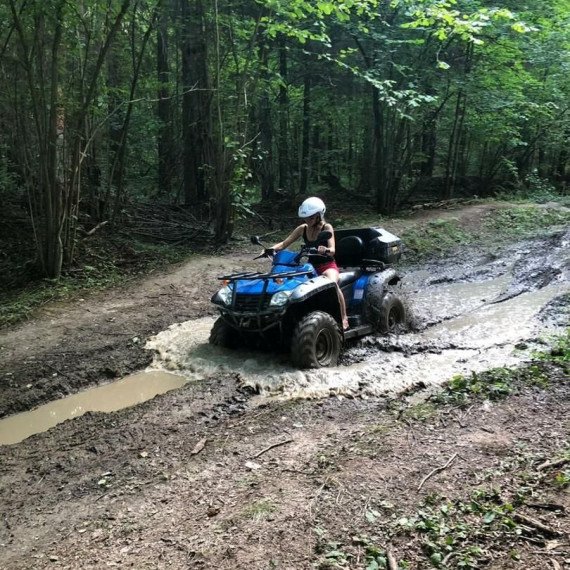 Мужчина на квадроцикле проезжает через лужу в лесу