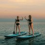 Две девушки на сапбордах приветствуют друг друга на воде во время заката - превью 1
