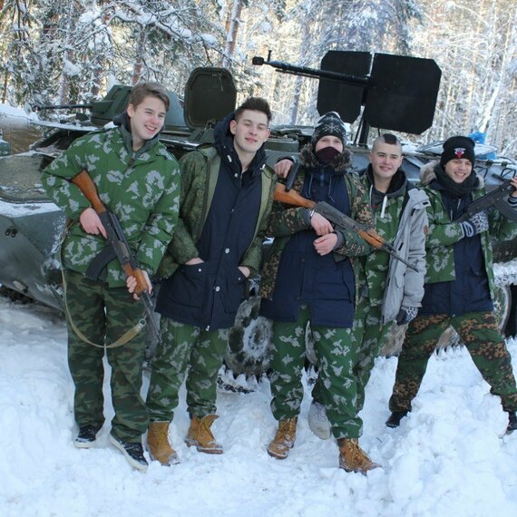 Молодые люди в зимней форме стоят у бронетранспортера в лесу, готовясь к учениям в холодную погоду рядом с солнечным светом