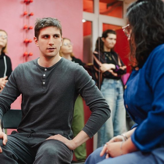 Молодые люди находятся на занятиях в студии. В комнате много участников, они общаются и изучают что-то новое