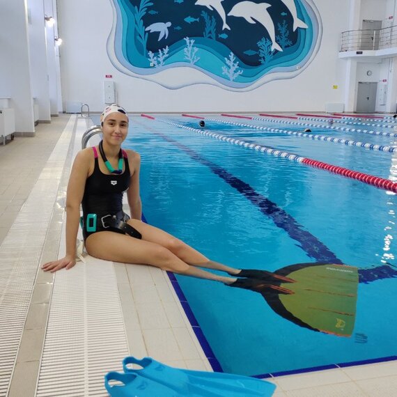 Женщина сидит у бассейна с ластами и готовится к тренировке по плаванию