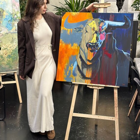 Женщина стоит рядом с картиной быка на художественной выставке в городе