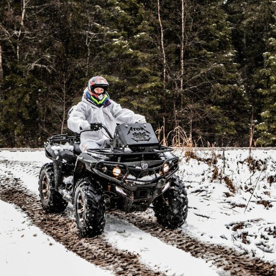 Квадроцикл движется по снежной дороге в лесу в холодный зимний день. Главное фото
