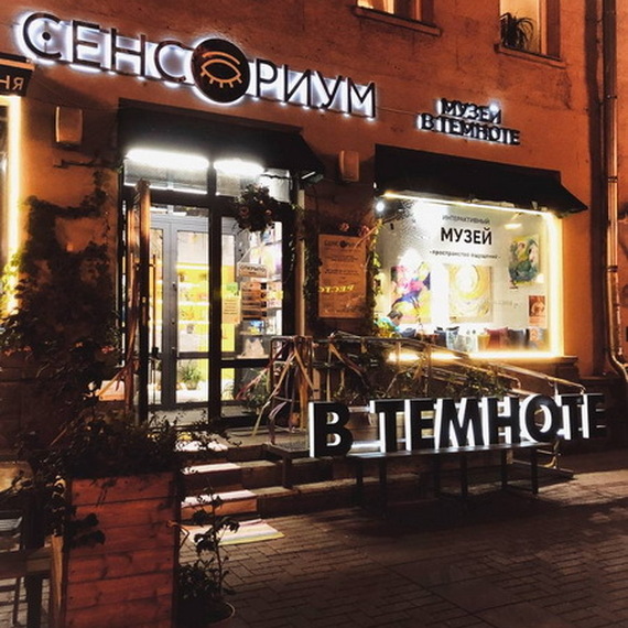 Сенсорный музей «В темноте» на улице в вечернее время, освещенный яркими огнями и притягивающий внимание прохожих. Фото 7