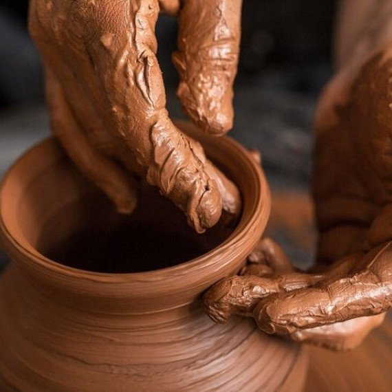 Руки формируют глиняный горшок на гончарном круге в мастерской. Главное фото