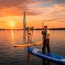 Два человека занимаются паддл-бордингом на реке в Санкт-Петербурге во время заката - превью 1