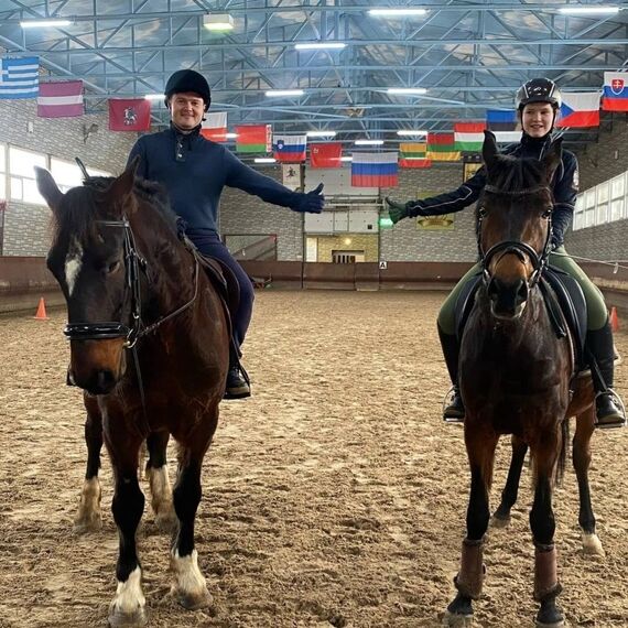 Урок верховой езды в крытом манеже с двумя всадниками и лошадьми в спортивной школе. Фото 6
