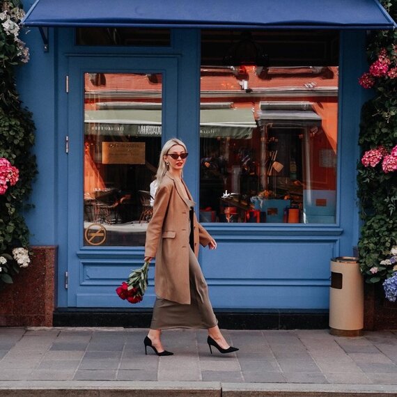 Женщина с цветами идет по улице возле кафе в день с ясным небом