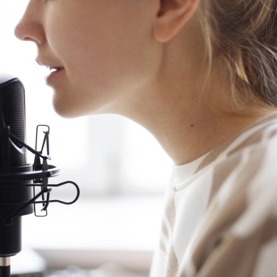 Женщина говорит в микрофон в комнате с окнами и светом, звукозапись проходит Женщина говорит в микрофон в комнате с окнами и светом, звукозапись проходит