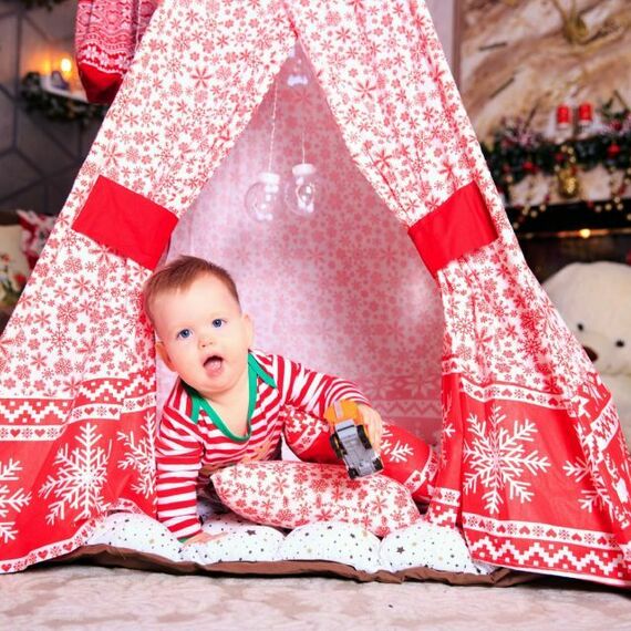 Младенец в новогоднем домике из ткани, играющий с игрушкой в уютной комнате с новогодним декором. Фото 5