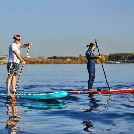 Два человека катаются на сапах на реке в солнечный день осенью Два человека катаются на сапах на реке в солнечный день осенью