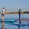 Два человека занимаются паддлбордингом на воде в ясный день возле города - превью 1