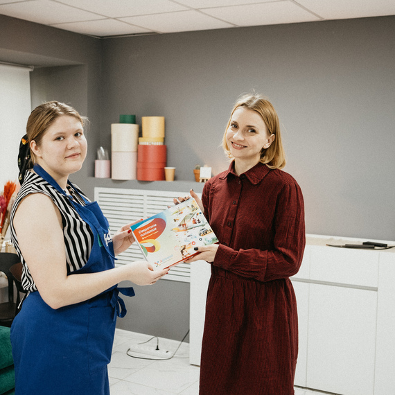 Две женщины обмениваются кулинарной книгой в уютном помещении на мастер-классе по кулинарии в центре города. Фото 15