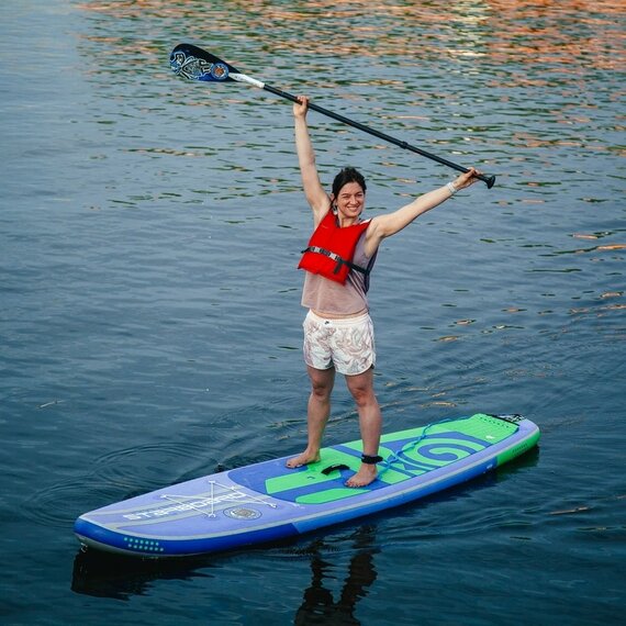 Женщина на доске для серфинга на веслах поднимает руки вверх, наслаждаясь солнечным днем на воде в городе