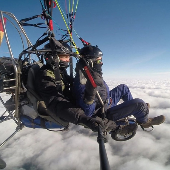 Полет на ультралайтере над облаками в ясный день, двое пилотов наслаждаются невероятным видом с высоты