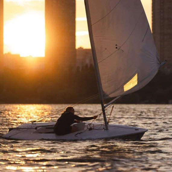 Человек в лодке с парусами в городе на закате