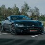 Красивый черный спорткар Aston Martin стоит на парковке среди зелени в солнечный день - превью 1