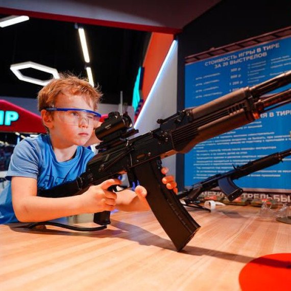 Мальчик стреляет из игрушечного автомата в тире Мальчик стреляет из игрушечного автомата в тире
