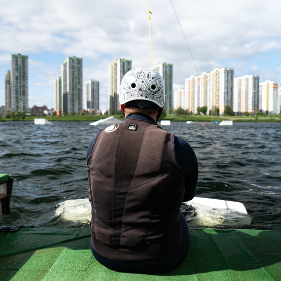 Человек на пирсе в жилом районе рядом с водоемом наблюдает за городской панорамой под облачным небом