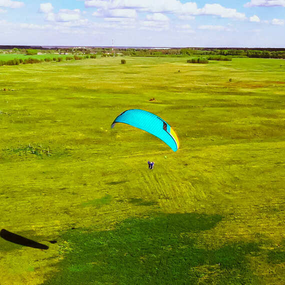 Парапланерист над зелеными полями в ясный день весной