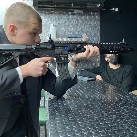 Человек в костюме целится из винтовки в помещении стрельбища. Главное фото